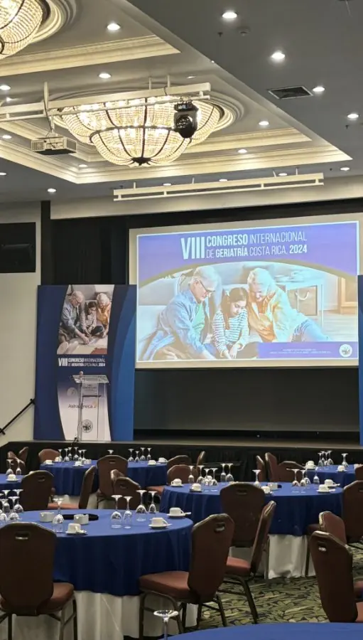 Sala plenaria de un congreso con pantalla central, tótems laterales y mesas de banquete